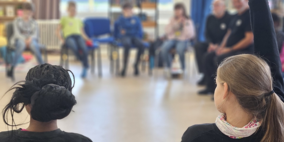 Jung trifft Alt Kinder und Erwachsene sitzen im Stuhlkreis, ein Kind meldet sich