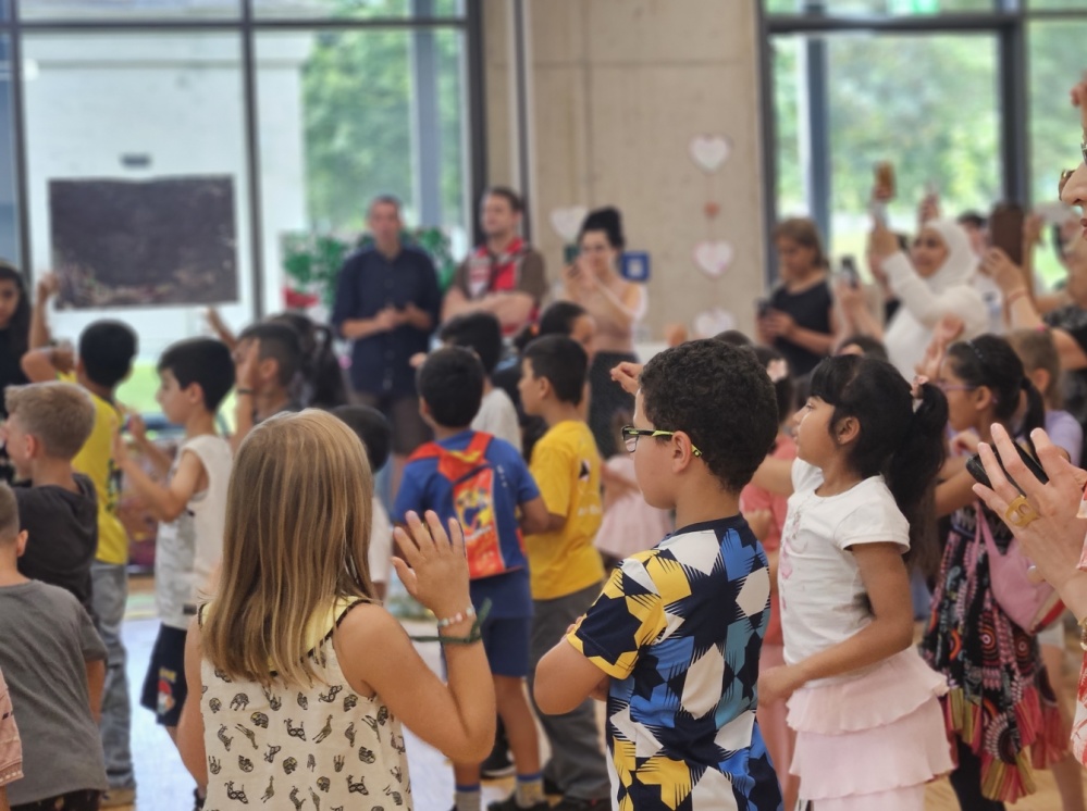Abschlussfeier Sprachcamp Gruppe von Kindern und Erwachsenen tanzen in Innenräumen der Bildungswerkstatt,