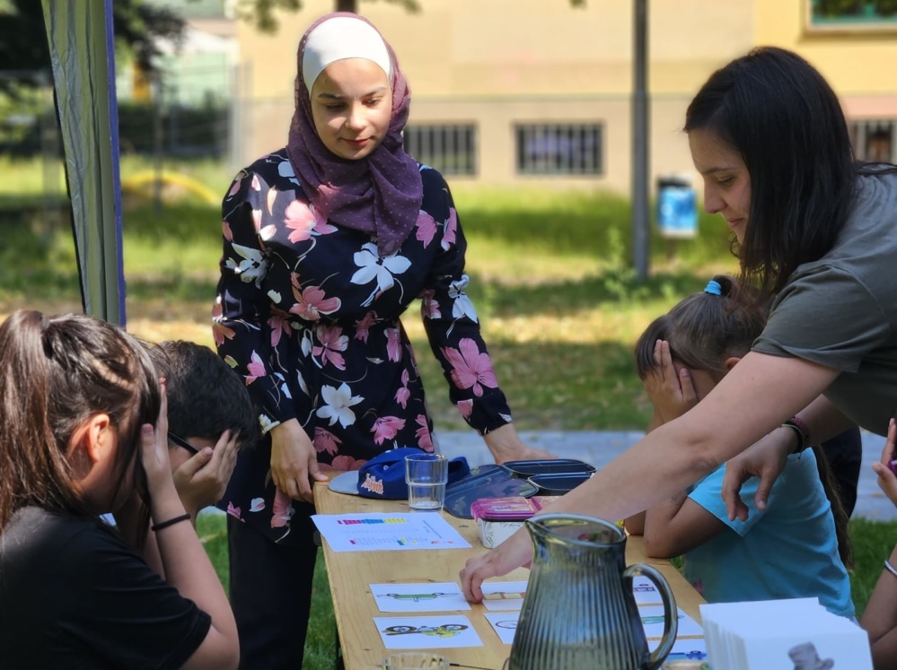 Sprachcamp 2024 Kinder sitzen am Tisch mit Bastelmaterial und Erwachsene legen Material aus