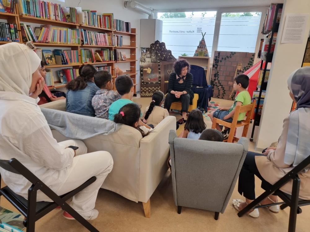 Kamishibai-Lesung im Kultur- und Lesetreff Gruppe von Kinder sitzt in Bibliothek, während Frau eine Geschichte erzählt