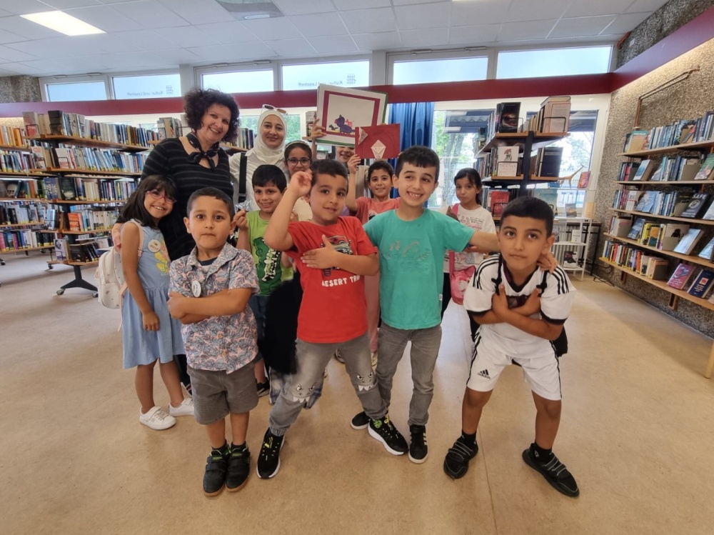 Kamishibai-Lesung im Kultur- und Lesetreff Gruppe von Kindern und Erwachsenen stehen in Bibliothek für Fotoaufnahme