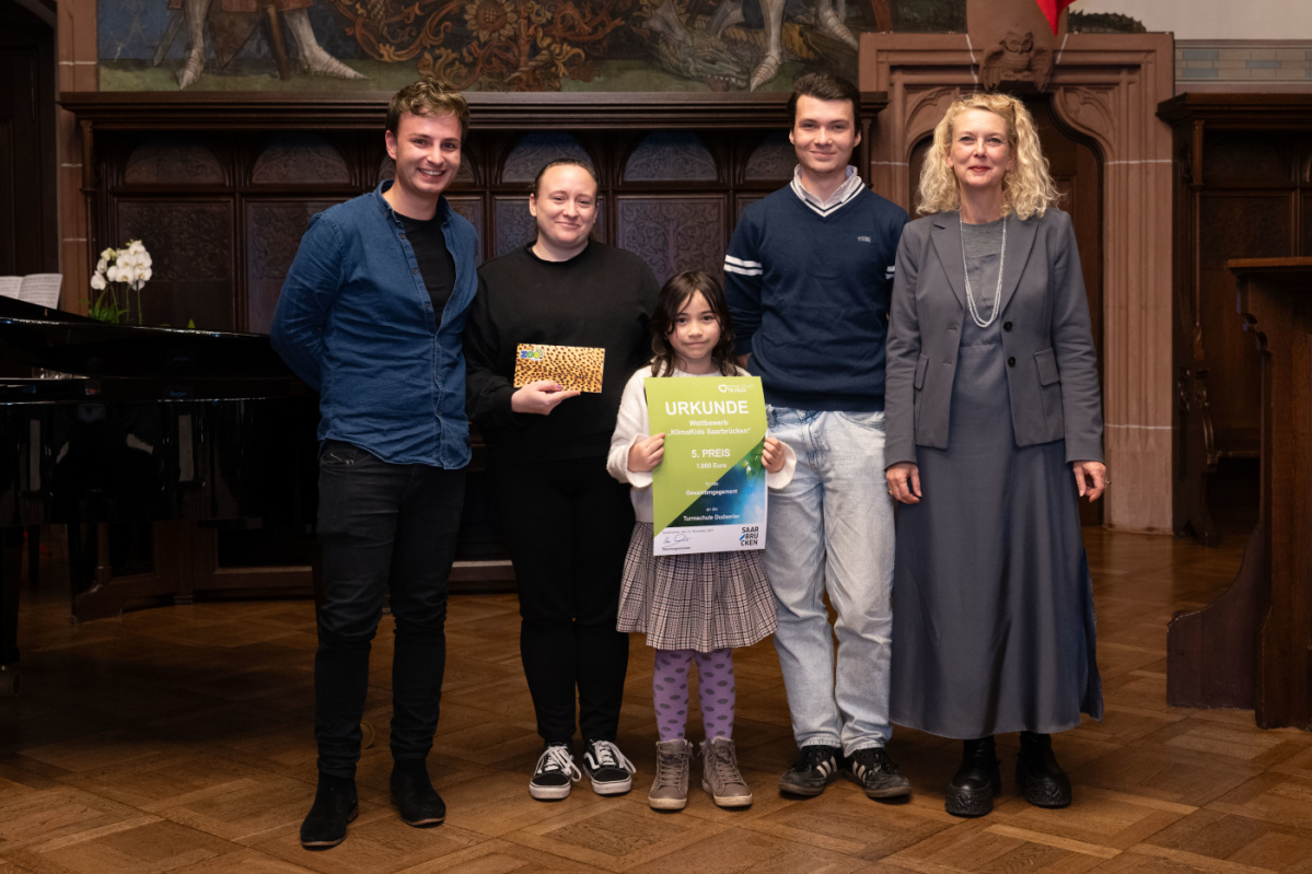 Platz 5 - Turmschule Dudweiler Preisübergabe des fünften Platzes an die Grundschule Dudweiler. Zu sehen ist eine Schülerin welche die Urkunde hält und zwei Betreuer der Grundschule, sowie zwei Jurymitglieder.