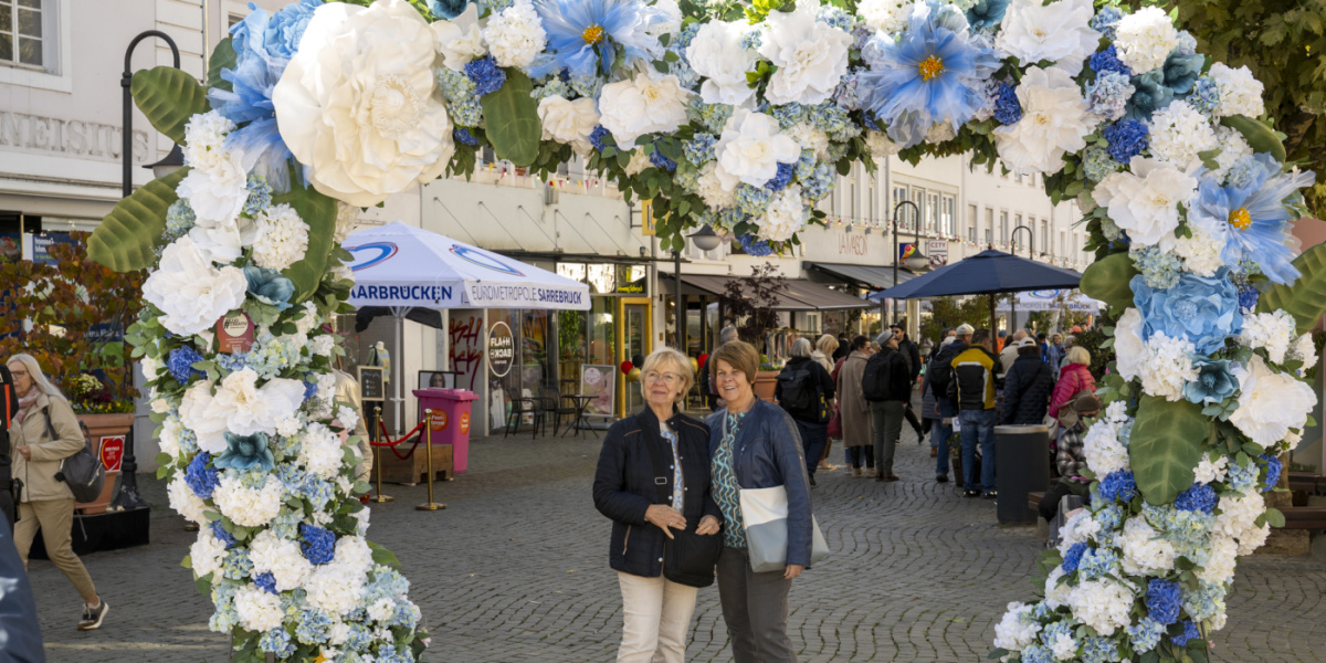 Zwei Frauen posieren unter Blumenbogen in der Innenstadt