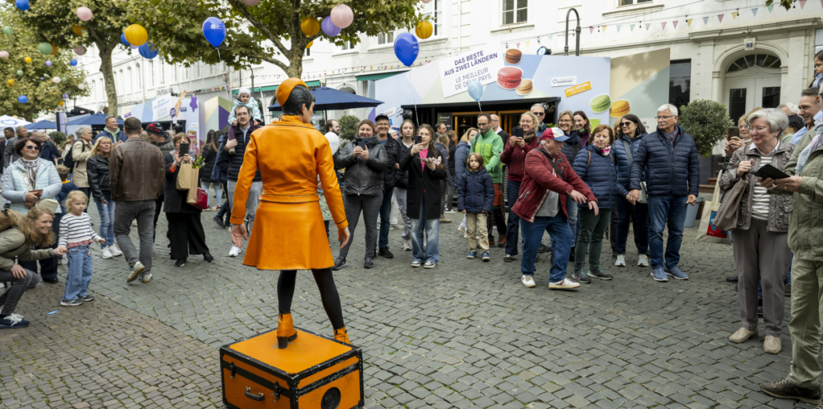 Publikum schaut Künstlerin in Orange auf Kiste an