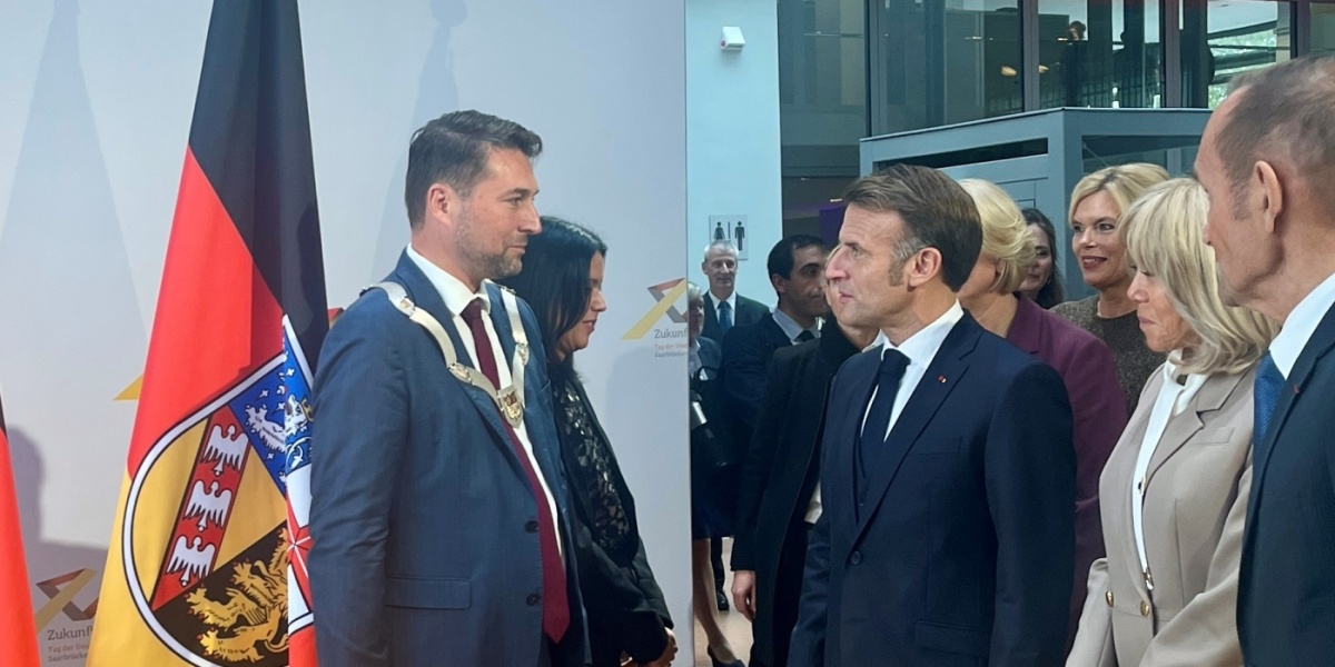 OB Uwe Conradt und der französische Präsident Emmanuel Macron stehen sich gegenüber, dahinter eine Saarland-Flagge