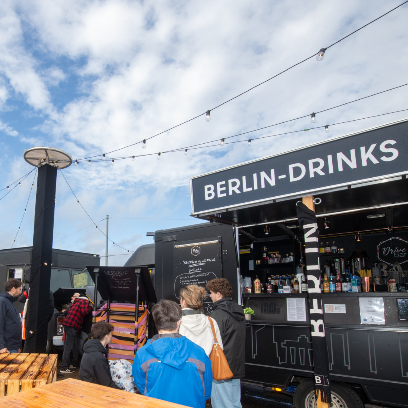 Streetfood-Bereich mit Foodtrucks, unter anderem „Berlin-Drinks“, Holztische und zahlreiche Besucher.